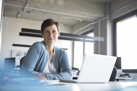 Portrait of smiling businesswoman in office with laptop stock photo