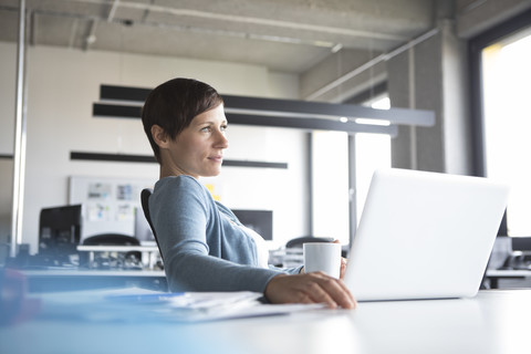 Geschäftsfrau im Büro mit Laptop denkt nach, lizenzfreies Stockfoto