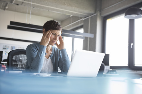 Businesswoman in office with head in hands using laptop stock photo