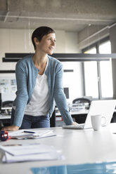 Lächelnde Geschäftsfrau, die sich auf einen Bürotisch stützt - RBF05267