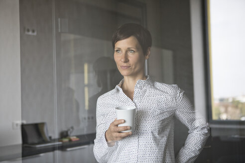 Lächelnde Frau mit einer Tasse Kaffee, die aus dem Fenster schaut - RBF05272