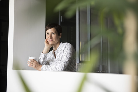 Lächelnde Frau mit einer Tasse Kaffee am Fenster, lizenzfreies Stockfoto