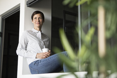 Lächelnde Frau mit einer Tasse Kaffee am Fenster - RBF05275