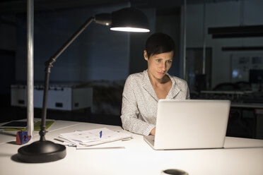 Businesswoman in office using laptop in the dark - RBF05276