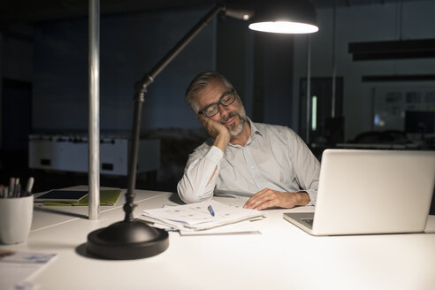 Exhausted businessman in office with laptop in the dark - RBF05279