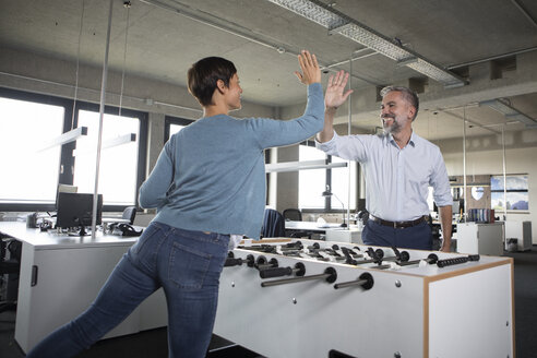 Zwei Kollegen spielen Tischfußball und geben sich im Büro die Hand - RBF05285