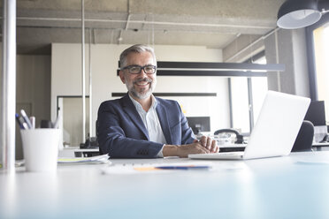 Smiling businessman using laptop in office - RBF05304