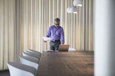 Businessman in boardroom with documents and laptop - RBF05324