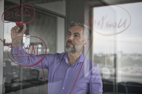 Businessman in office writing on glass wall - RBF05332