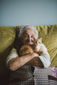 Porträt einer glücklichen älteren Frau, die mit ihrer Katze auf der Couch kuschelt - RAEF01593