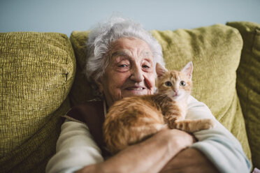 Portrait of happy senior woman cuddling with her cat on the couch - RAEF01594