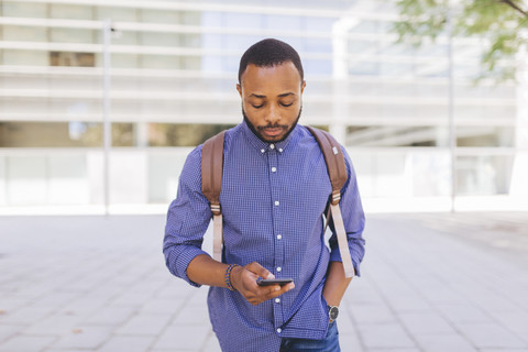 Mann mit Rucksack schaut auf sein Handy, lizenzfreies Stockfoto