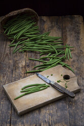 Wickerbasket, green beans, wooden board and pocket knife on dark wood - LVF05643
