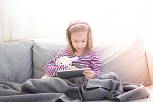 Porträt eines kleinen Mädchens, das auf der Couch sitzt und ein Tablet benutzt - LVF05649