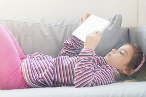 Kleines Mädchen auf der Couch liegend mit Tablet, lizenzfreies Stockfoto