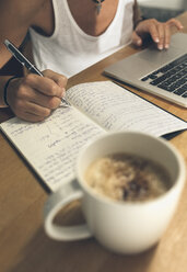 Woman with laptop at desk writing in book - MGOF02662