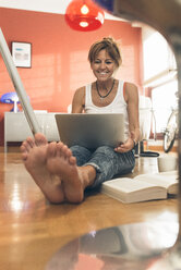 Lächelnde Frau zu Hause auf dem Boden sitzend mit Laptop - MGOF02669