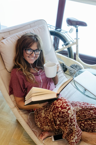 Lächelnde Frau, die zu Hause ein Buch liest, lizenzfreies Stockfoto