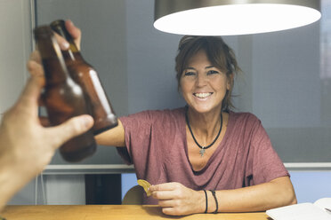 Lächelnde Frau, die auf eine Bierflasche anstößt - MGOF02683