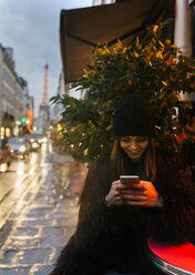 Frankreich, Paris, junge Frau schaut auf ihr Handy, im Hintergrund der Eiffelturm - MGOF02687