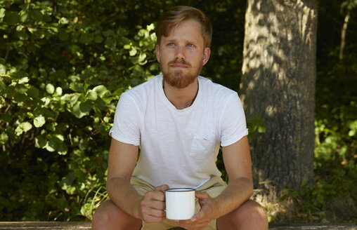 Junger Mann hält einen Becher in der Natur - FMKF03272