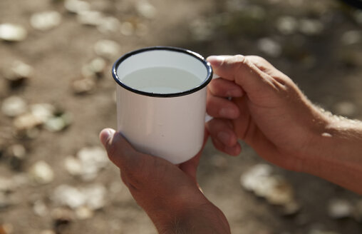 Hände halten Emaillebecher mit Wasser - FMKF03273