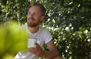 Lächelnder junger Mann mit einem Becher in der Natur - FMKF03274