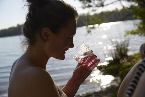 Lächelnde junge Frau an einem See beim Trinken - FMKF03277