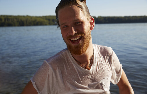 Glücklicher junger Mann mit nassem T-Shirt an einem See - FMKF03281