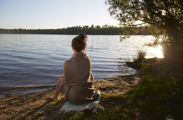 Junge Frau sitzt bei Sonnenuntergang an einem See - FMKF03290