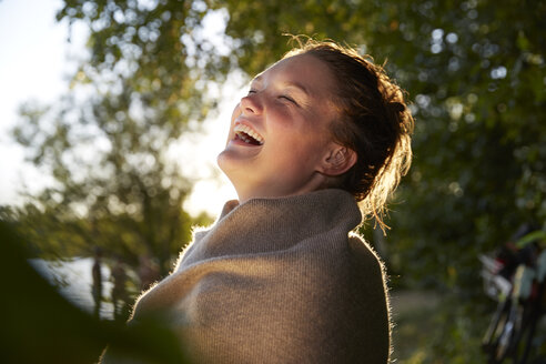 Lachende junge Frau, eingewickelt in eine Decke bei Sonnenuntergang - FMKF03294