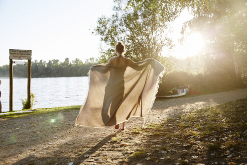 Junge Frau hält eine Decke an einem See bei Sonnenuntergang - FMKF03295