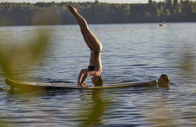 Frau macht einen Handstand auf einem Paddleboard in einem See - FMKF03305