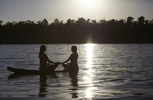 Zwei Frauen machen Yoga auf dem Paddleboard bei Sonnenuntergang - FMKF03306