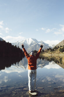 France, Pyrenees, Pic Carlit, hiker raising his arms at mountain lake - KKAF00164