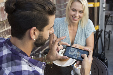 Junger Mann mit Freundin, der ein Handyfoto in einem Café im Freien macht - WEST22140