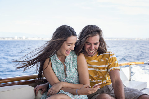 Glückliches Paar auf einer Bootsfahrt mit Blick auf das Mobiltelefon, lizenzfreies Stockfoto