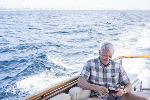 Älterer Mann auf einer Bootsfahrt schaut auf sein Handy - WESTF22227