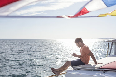 Young man sitting on a boat looking at cell phone - WESTF22260