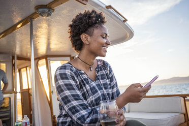 Smiling young woman on a boat checking cell phone - WESTF22278