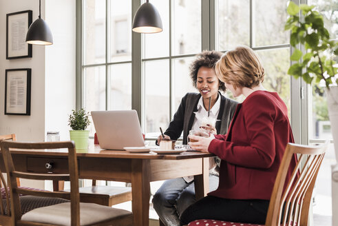 Zwei junge Frauen benutzen einen Laptop in einem Cafe - UUF09441