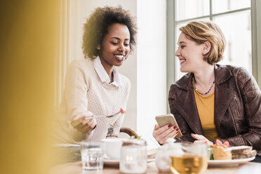 Two young women with cell phone meeting in a cafe - UUF09460