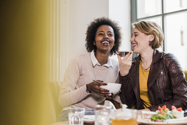 Zwei glückliche junge Frauen telefonieren in einem Cafe - UUF09464