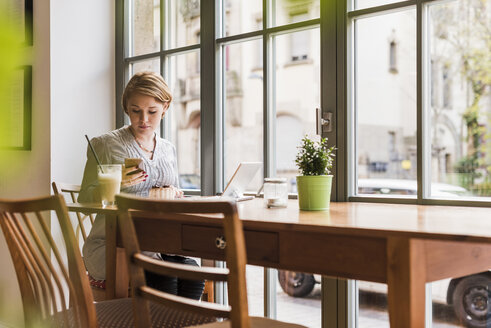 Junge Frau mit Handy und Tablet in einem Cafe - UUF09477