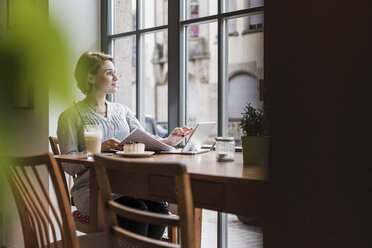 Junge Frau mit Tablet in einem Café und Blick aus dem Fenster - UUF09479