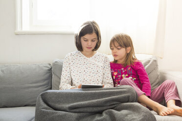 Girl sitting on the couch using mini tablet while her sister watching her - LVF05673