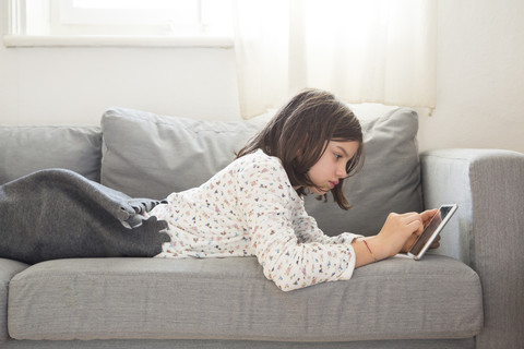 Mädchen auf der Couch liegend mit Mini-Tablet, lizenzfreies Stockfoto