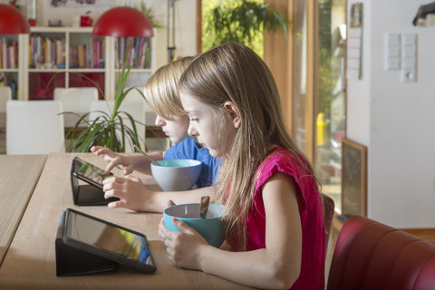 Junge und Mädchen benutzen Tabletten am Frühstückstisch, lizenzfreies Stockfoto