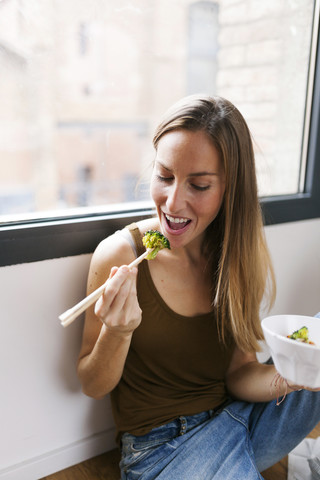 Frau zu Hause isst Gemüse mit Stäbchen, lizenzfreies Stockfoto