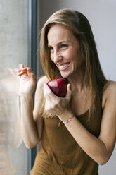 Frau steht am Fenster und isst einen Apfel - VABF00900